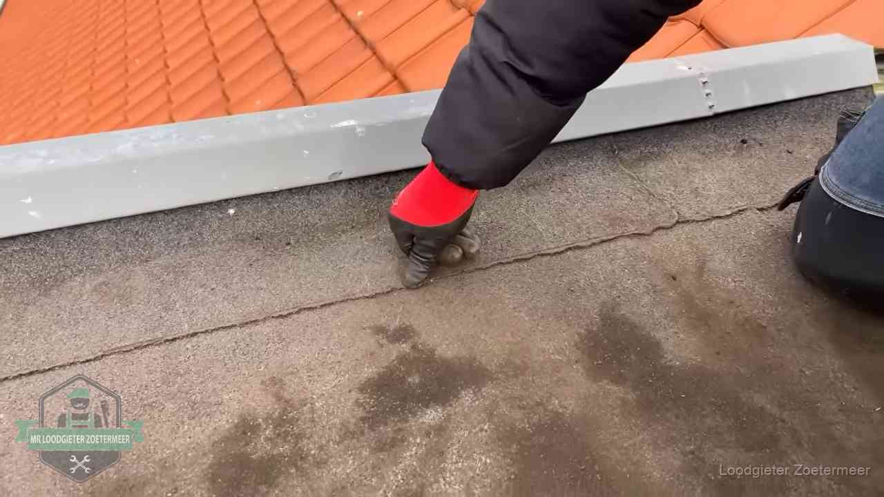 Vakman wijst een naad met vochtplekken aan op een bitumen plat dak in Zoetermeer
