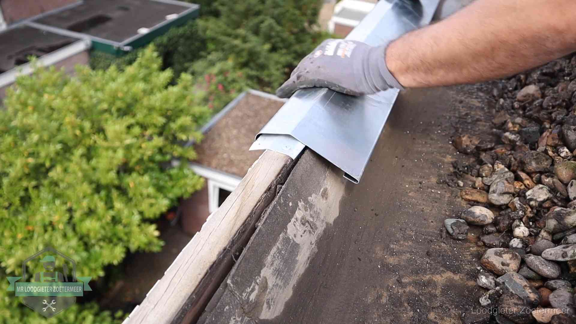 Dakdekker plaatst een zinken deklijst op een dakrand met uitzicht over een woonwijk in Zoetermeer