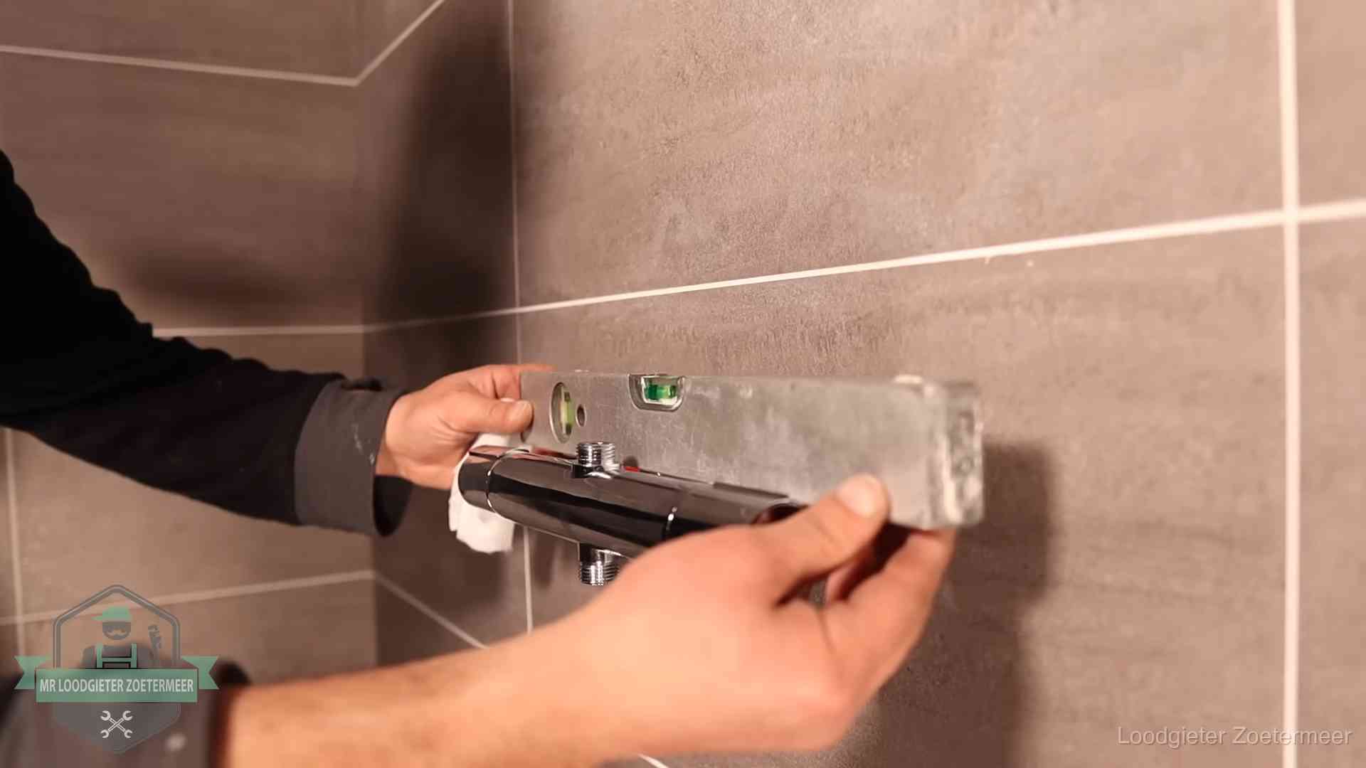Loodgieter lijnt een douchekraan uit met een waterpas in een woning in Zoetermeer