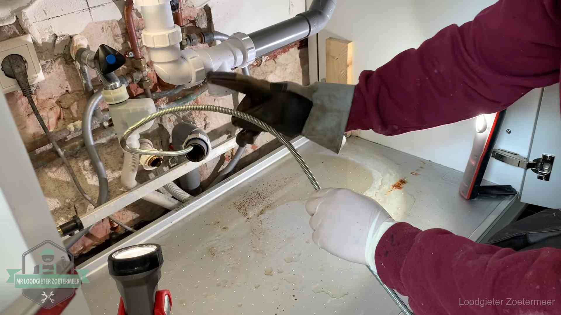 Ontstoppingsveer gaat in een geopende sifonaansluiting onder het aanrecht in Zoetermeer