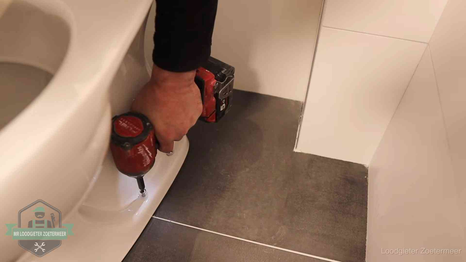 Kosten wc ontstoppen in Zoetermeer Loodgieter zet de voet van een wc-pot vast op de tegelvloer in Zoetermeer